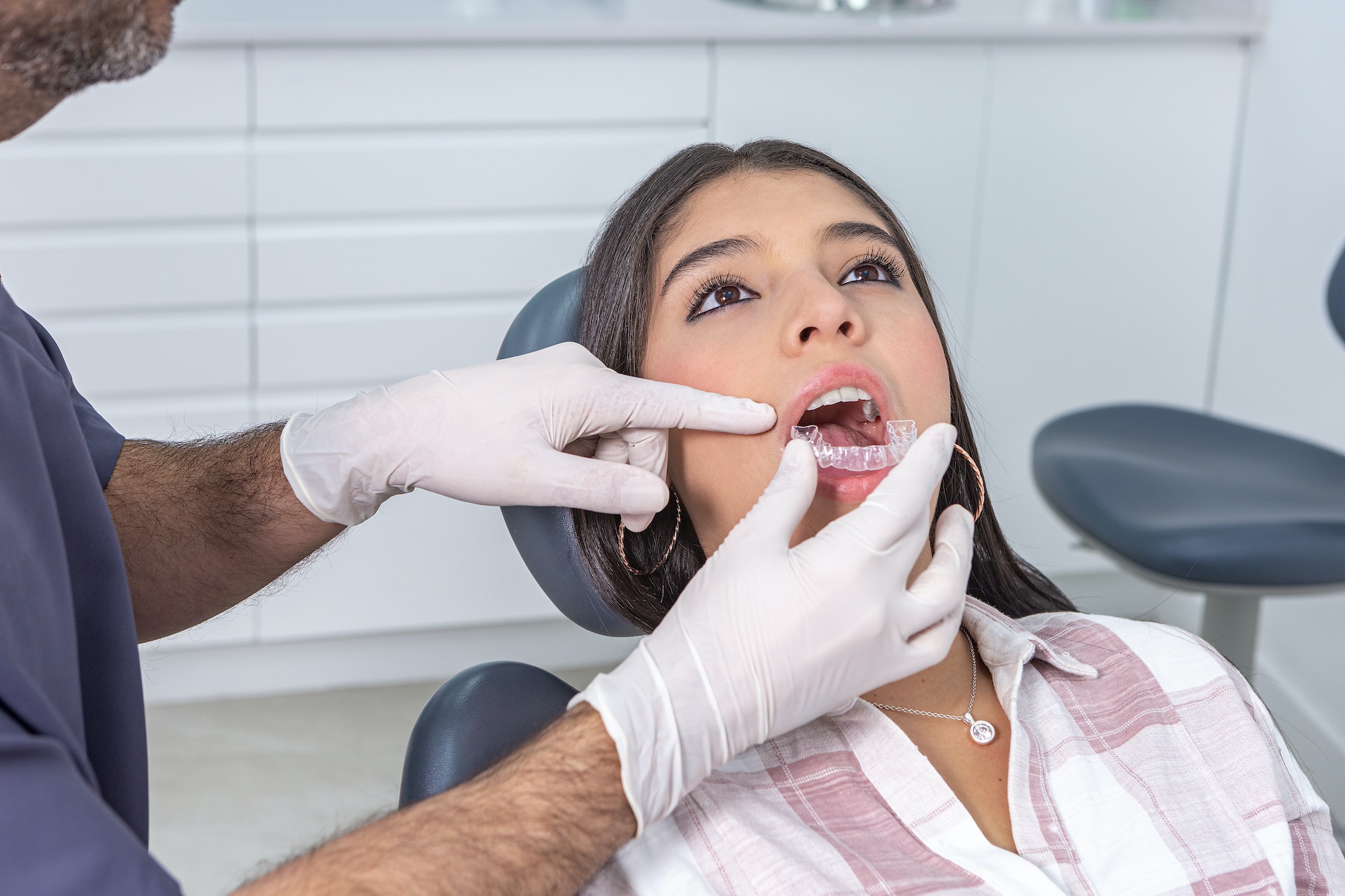 Crop male stomatologist fitting dental aligners on female patient teeth